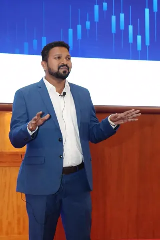 Dharanidharan speaking on stage in front of a candlestick chart
